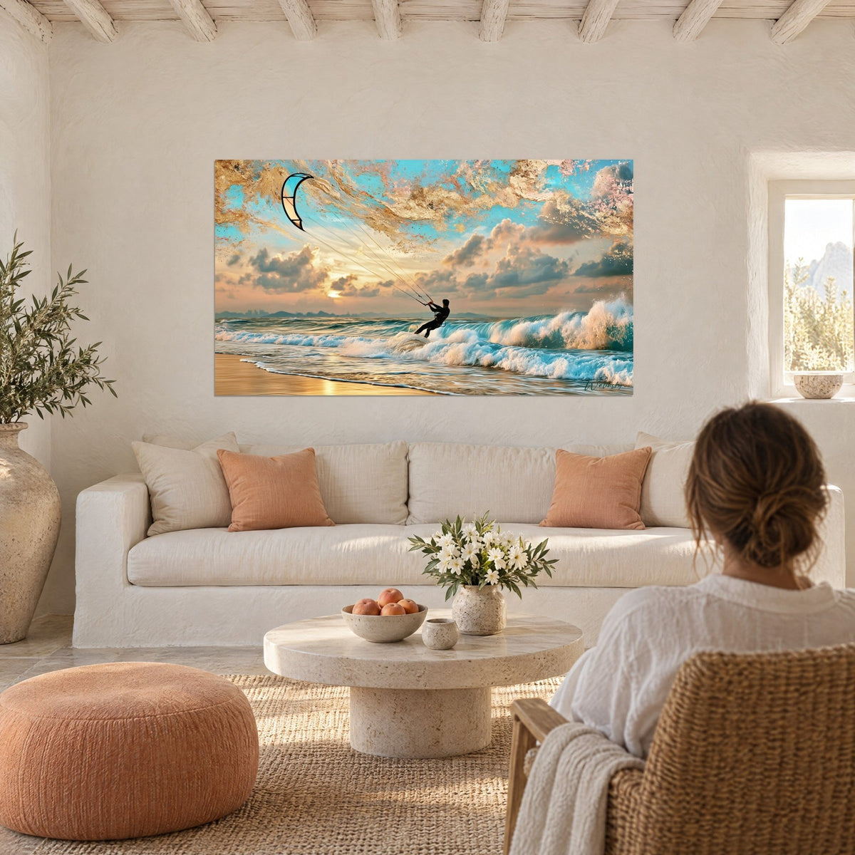 Quadro di un kitesurfer in muta nera su un'onda turchese, cielo oro e rosa, due persone di spalle, sopra un divano in un soggiorno luminoso