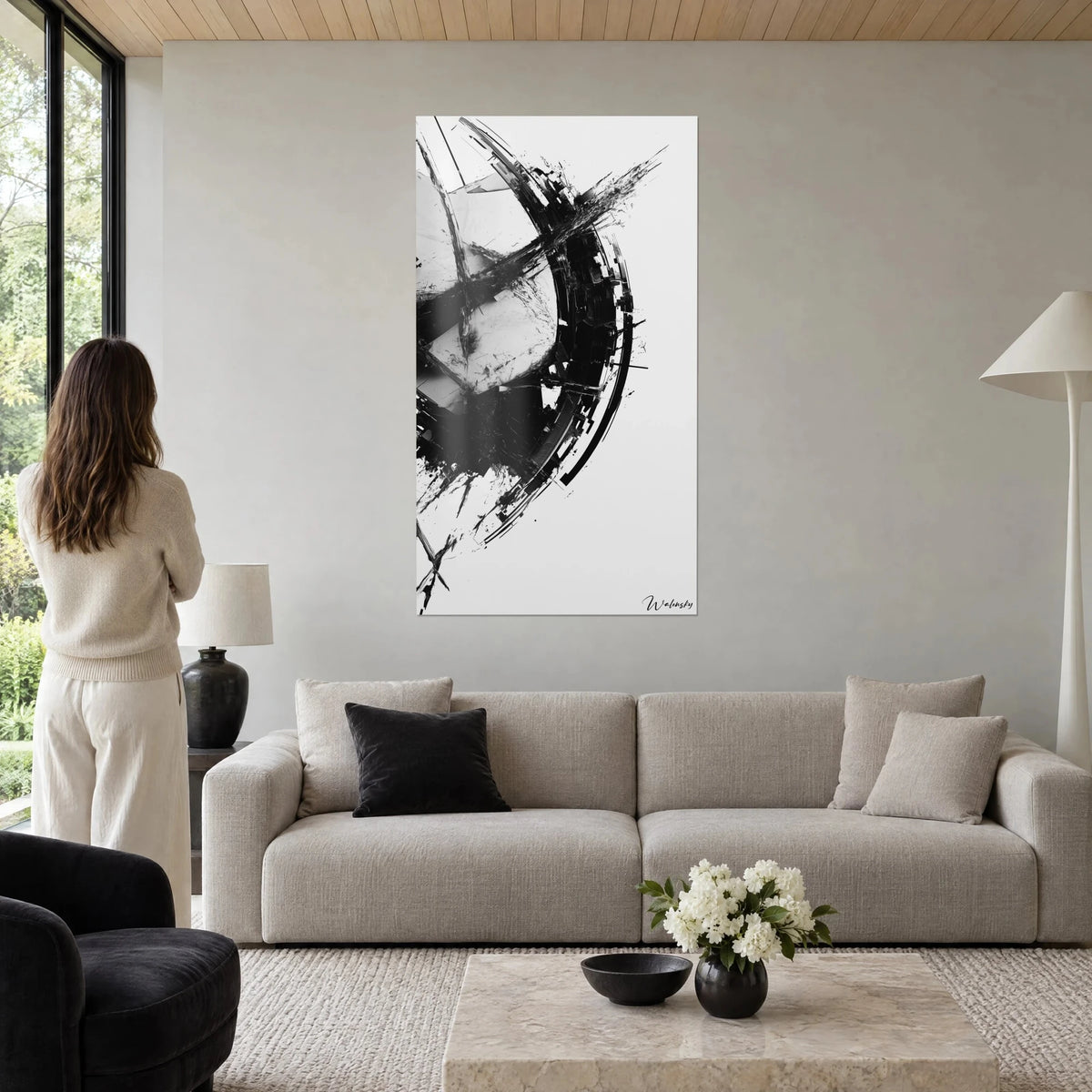 Wall art with a black brushstroke in a broken arc on white background, ink splashes, woman seen from behind, above a sofa in a bright living room