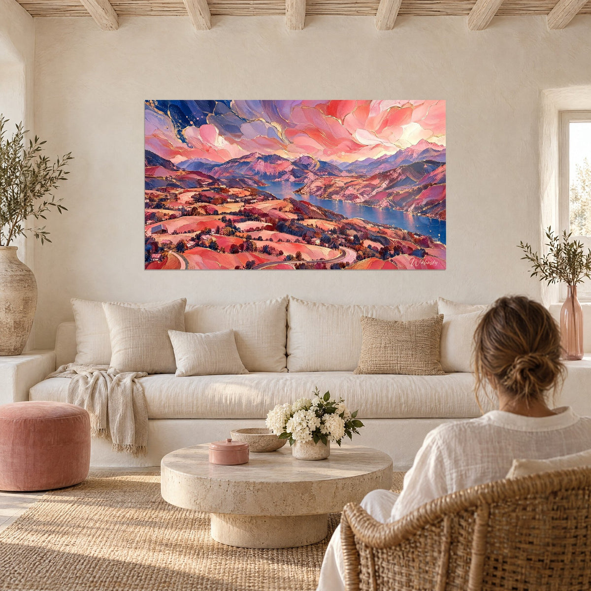 Quadro paesaggio di lago visto dall'alto, nuvole color corallo e colline rosa, blu navy, sopra un divano in un soggiorno luminoso