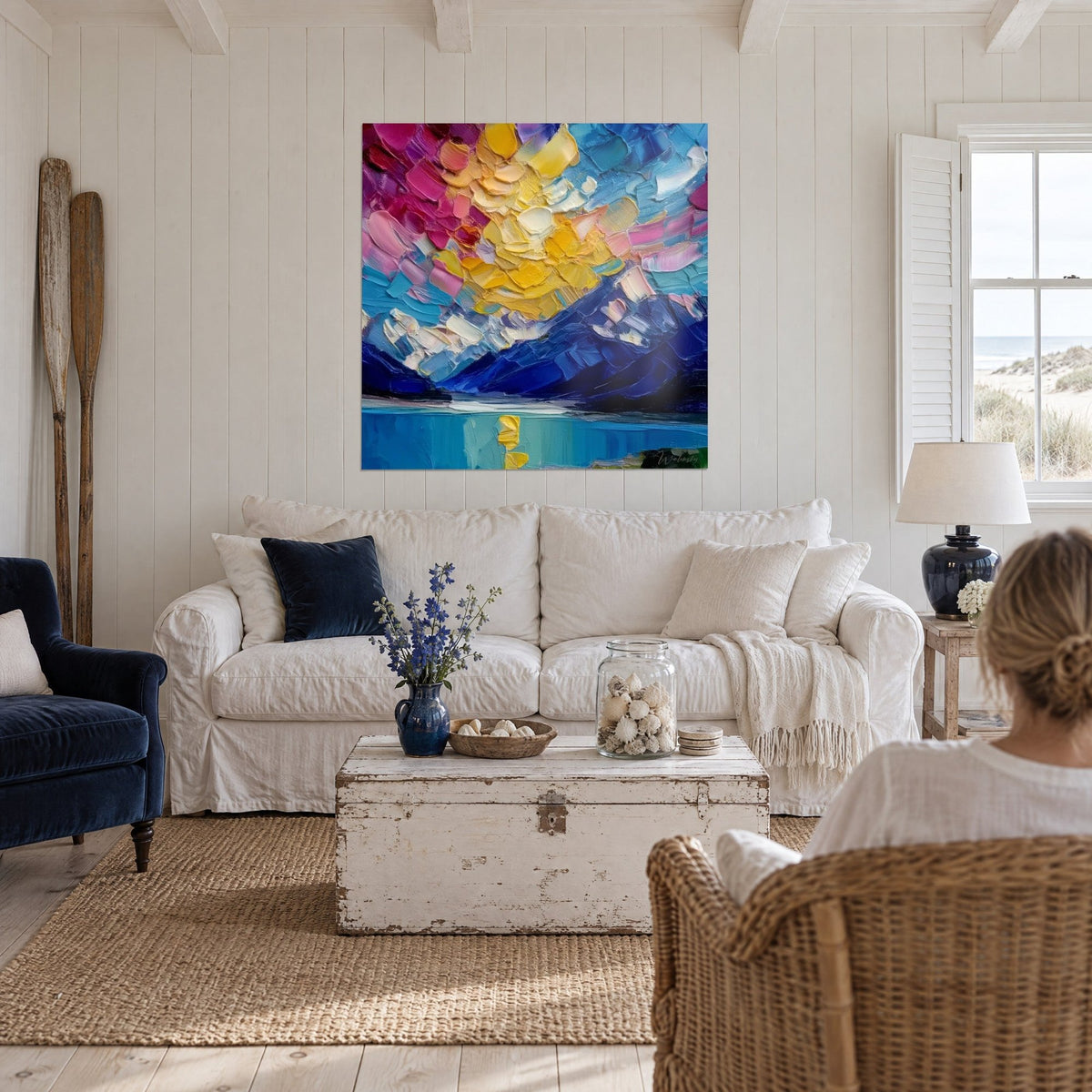 Tableau ciel jaune beurre et rose fuchsia en larges coups de couteau sur montagnes indigo, au-dessus d'un canapé dans un salon lumineux