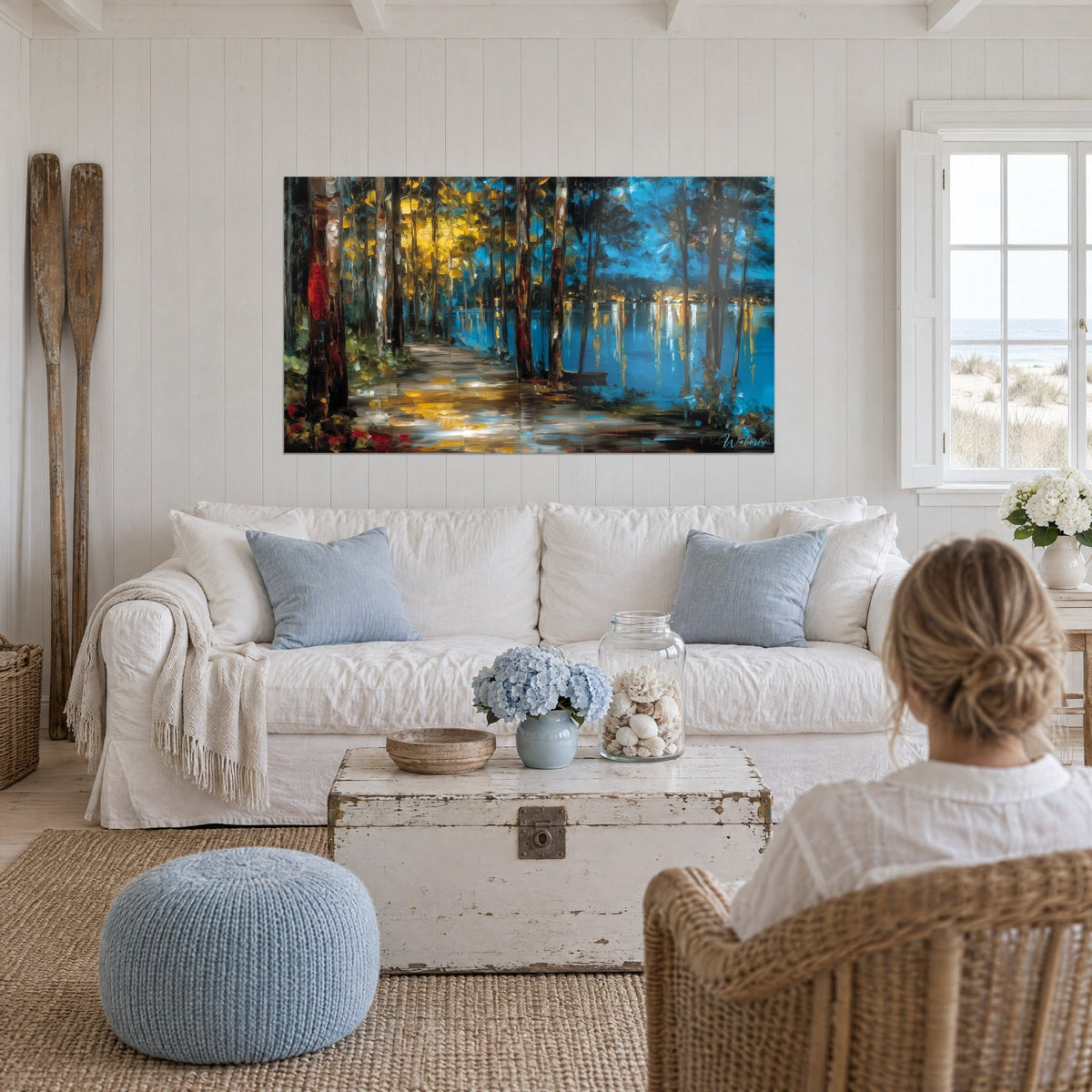 Wall art forest path along a blue lake, ochre and yellow reflections on the water, above a sofa in a bright living room