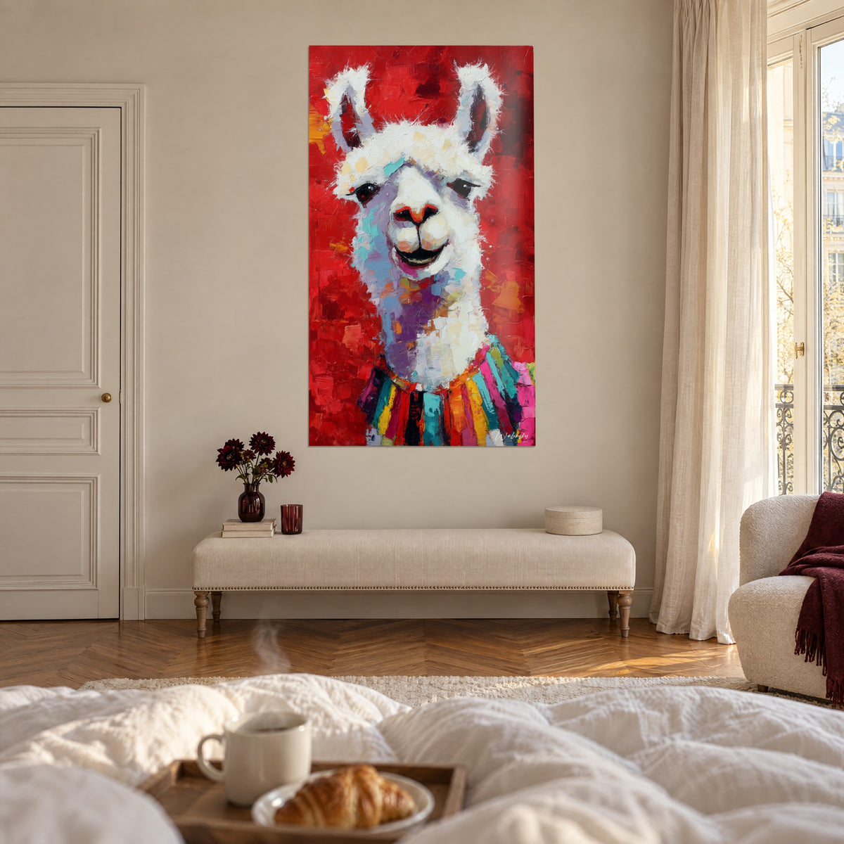 Cuadro de camélido alegre, hocico blanco y crema sobre fondo rojo, flecos multicolores, frente a un plato de croissants, encima de una cama en un dormitorio luminoso