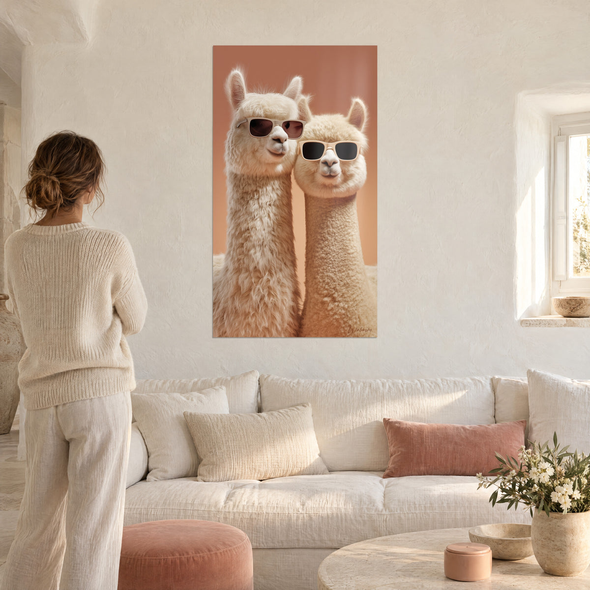 Gemälde zwei Alpakas mit Sonnenbrille, cremefarbenes Fell und terrakottafarbener Hintergrund, Frau von hinten über einem Sofa in einem hellen Wohnzimmer