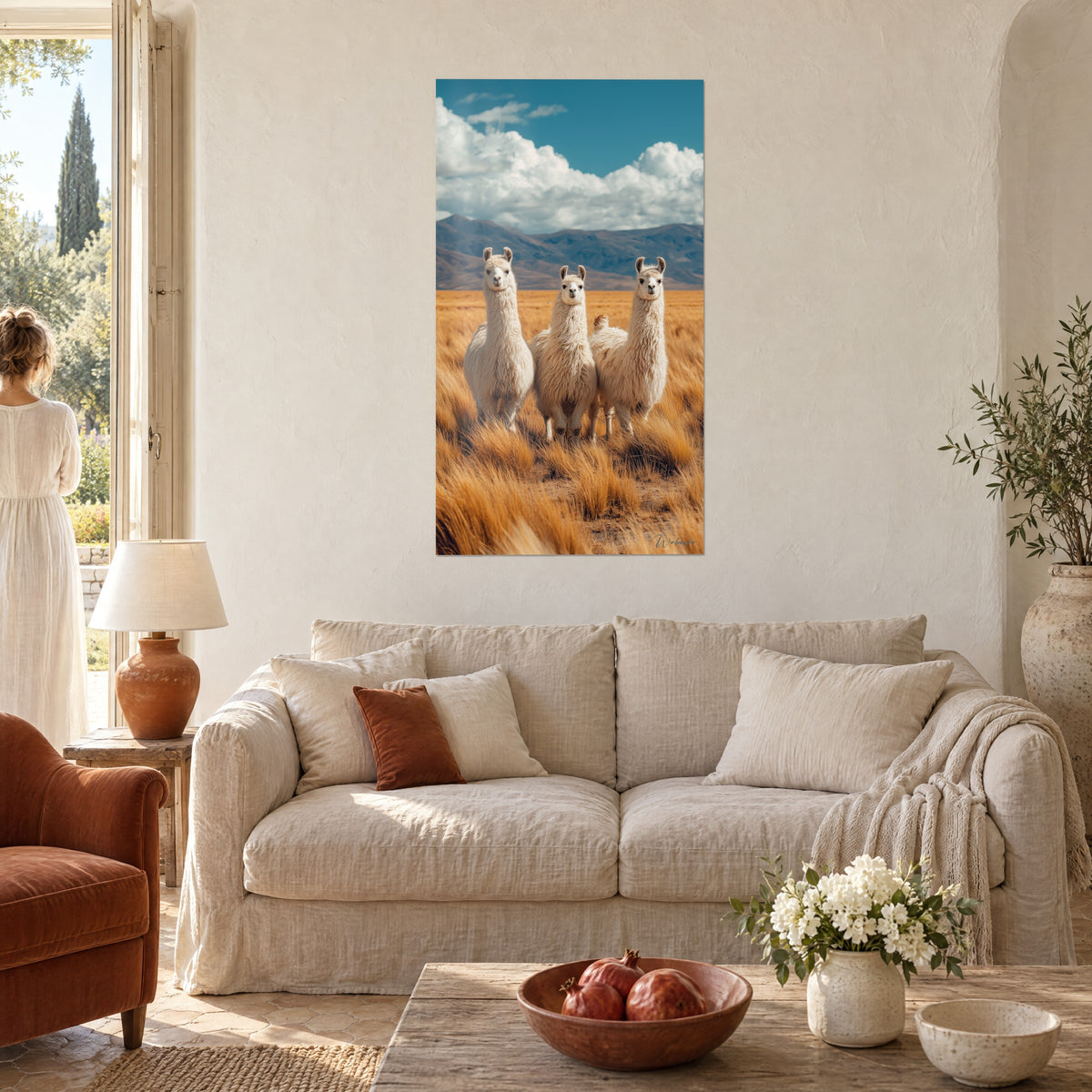 Cuadro tres llamas de lana crema erguidas sobre la hierba dorada, cielo azul y nubes, encima de un sofá en un salón luminoso