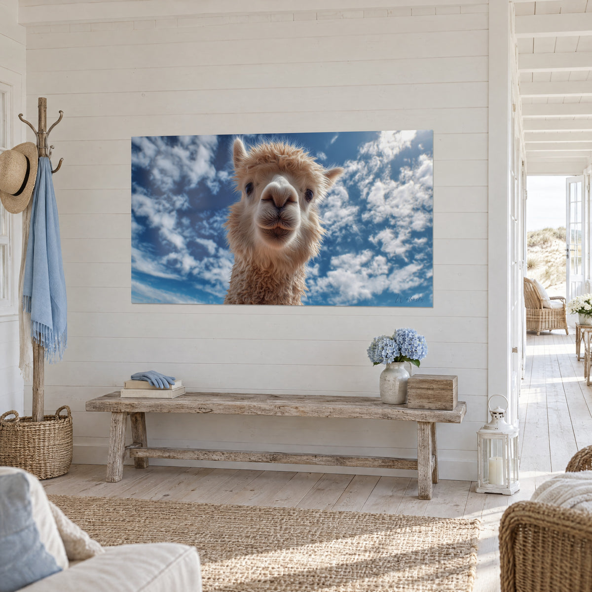 Cuadro de alpaca de orejas erguidas y vellón beige, nubes algodonosas sobre azul celeste, en un recibidor blanco junto a un banco