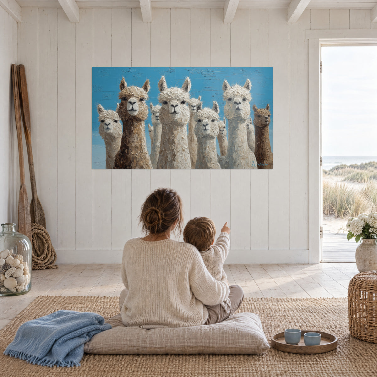Wall art family of white and brown llamas facing an azure sky, mother and child seated from behind on a cushion, seaside house