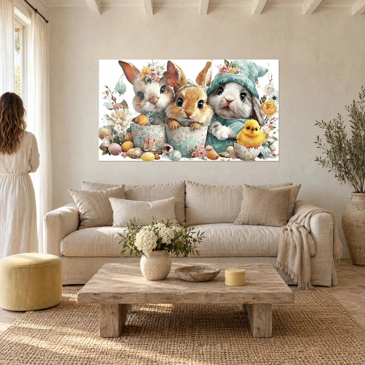 Quadro di tre coniglietti soffici e un pulcino giallo tra fiori e uova pastello, appeso sopra un divano in un soggiorno luminoso