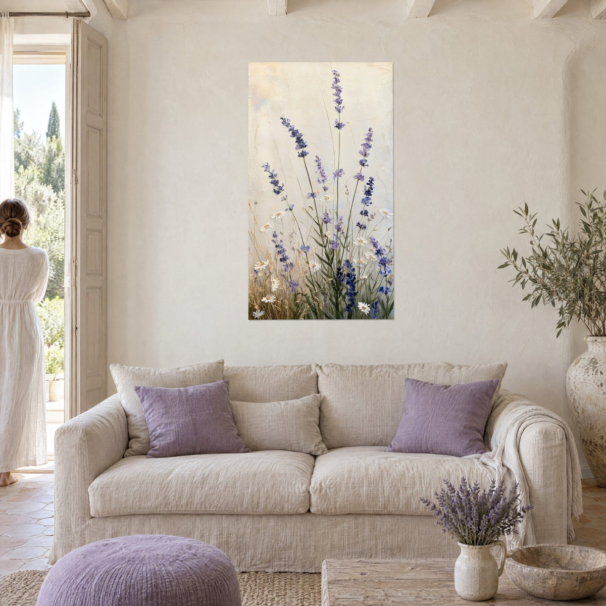 Quadro spighe di lavanda viola e margherite bianche su sfondo crema, donna di spalle, sopra un divano in un soggiorno luminoso
