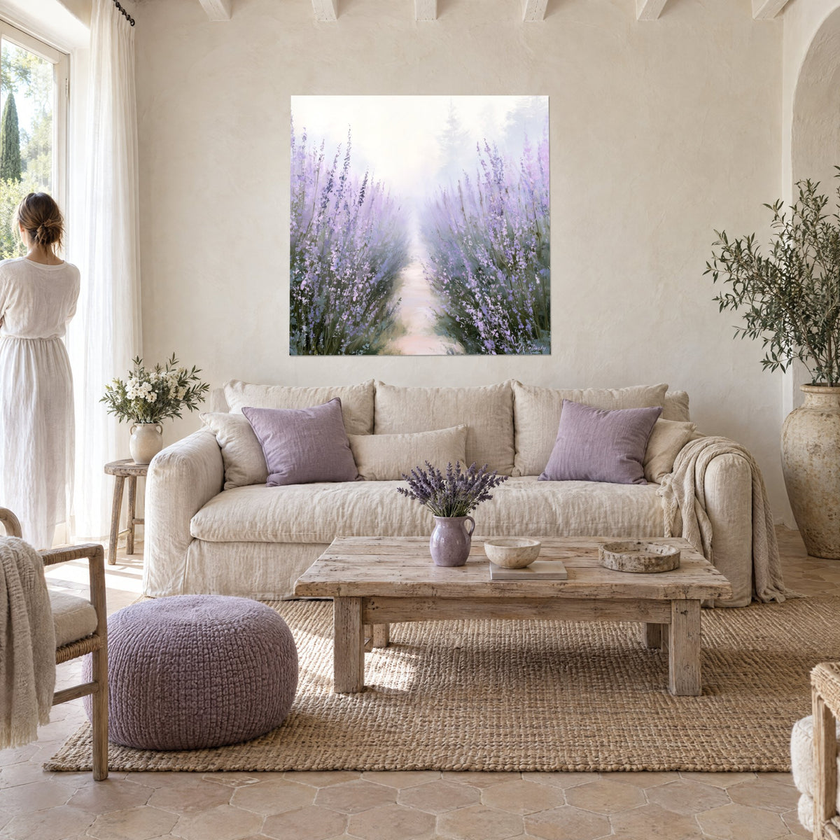 Wall art lavender field in purple bloom, misty path and pale pink ground, woman in white dress above a sofa in a bright living room