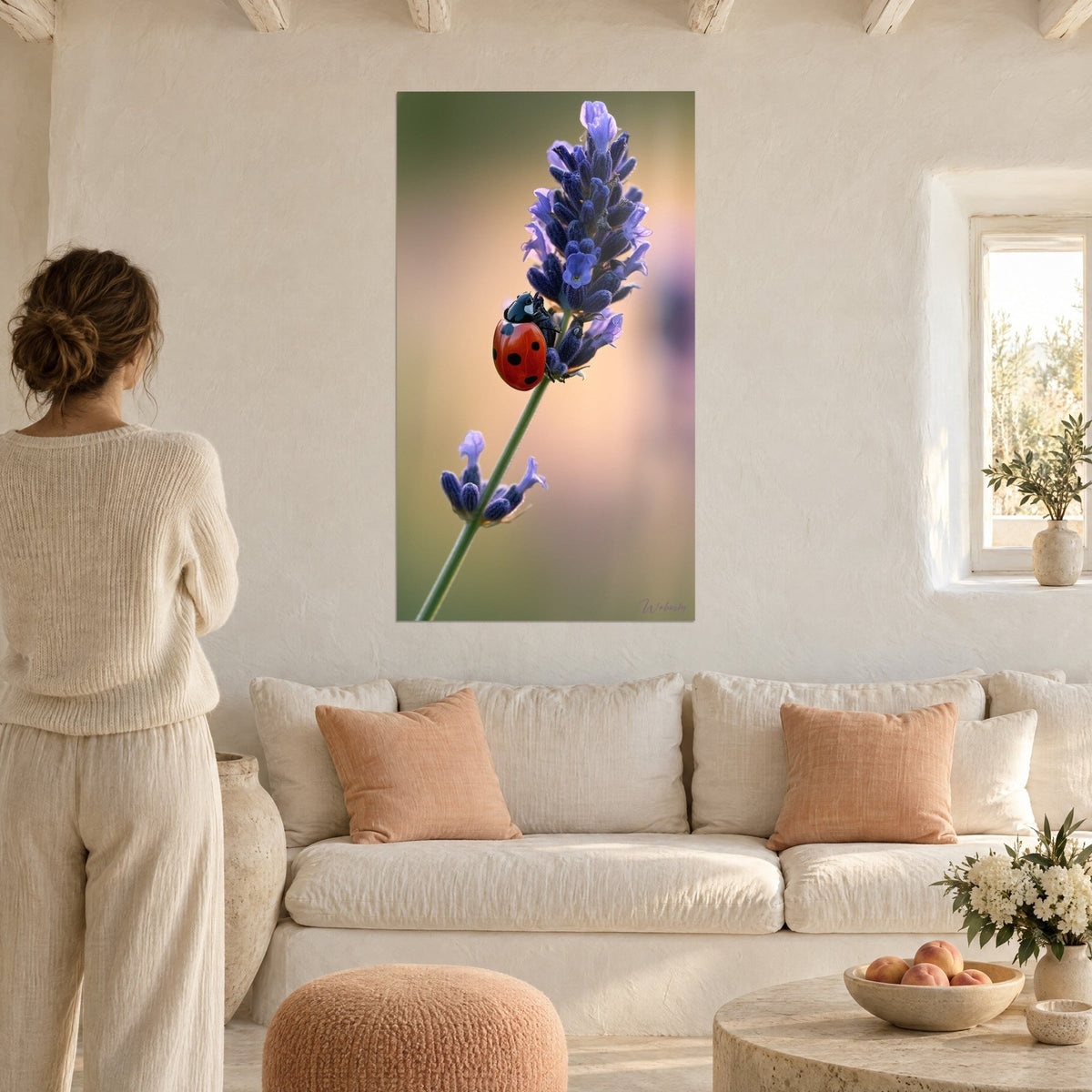 Wall art red ladybug with black spots on a purple lavender spike, blurred pink background, above a sofa in a bright living room