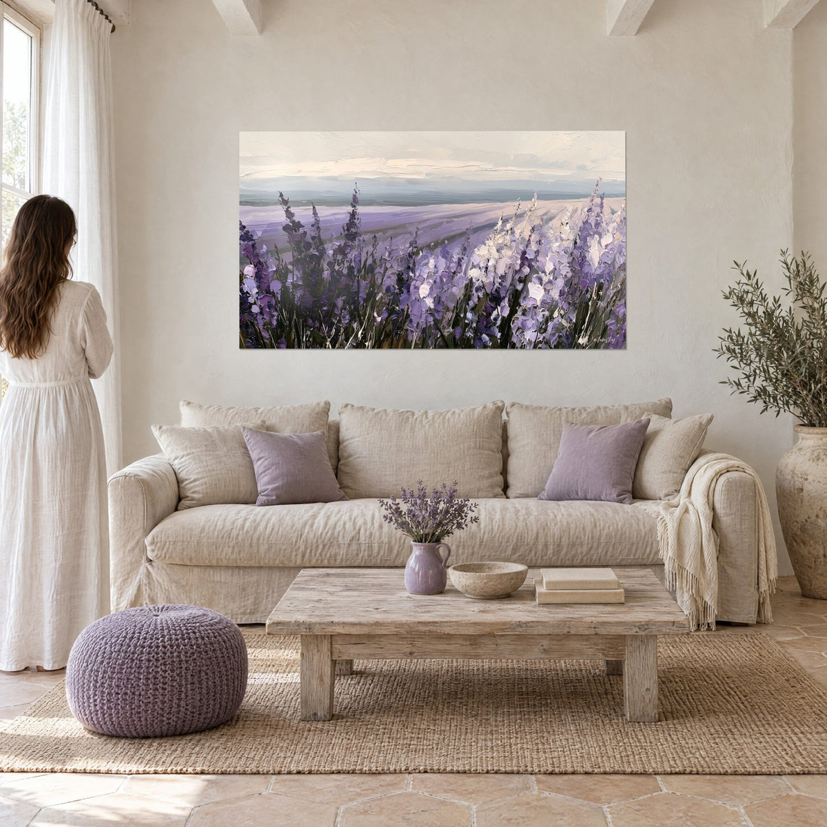Quadro campo di lavanda dipinto a spatola, spighe viola e bianche sotto un cielo color crema, donna di spalle, sopra un divano in un soggiorno luminoso