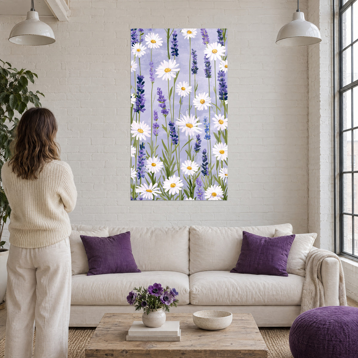Cuadro margaritas blancas de corazón dorado y espigas de lavanda violeta sobre fondo lila, mujer de espaldas, encima de un sofá en un salón luminoso
