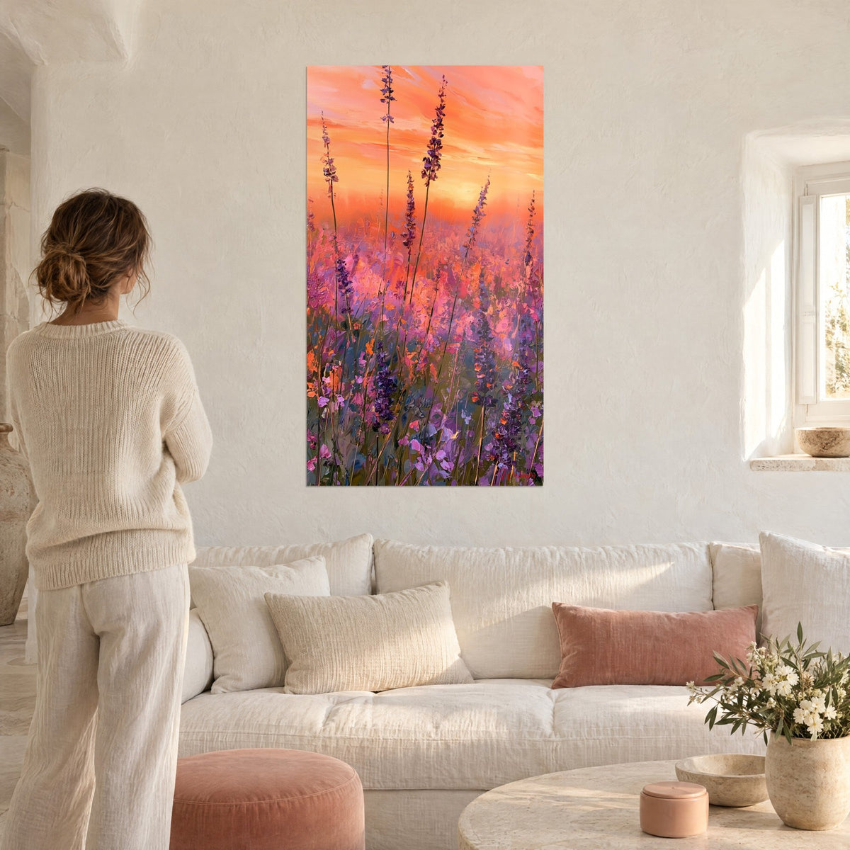Gemälde Lavendelfeld unter aprikosenfarbenem Himmel, violette Ähren und rosa Tupfer, Frau von hinten, über einem Sofa in einem hellen Wohnzimmer