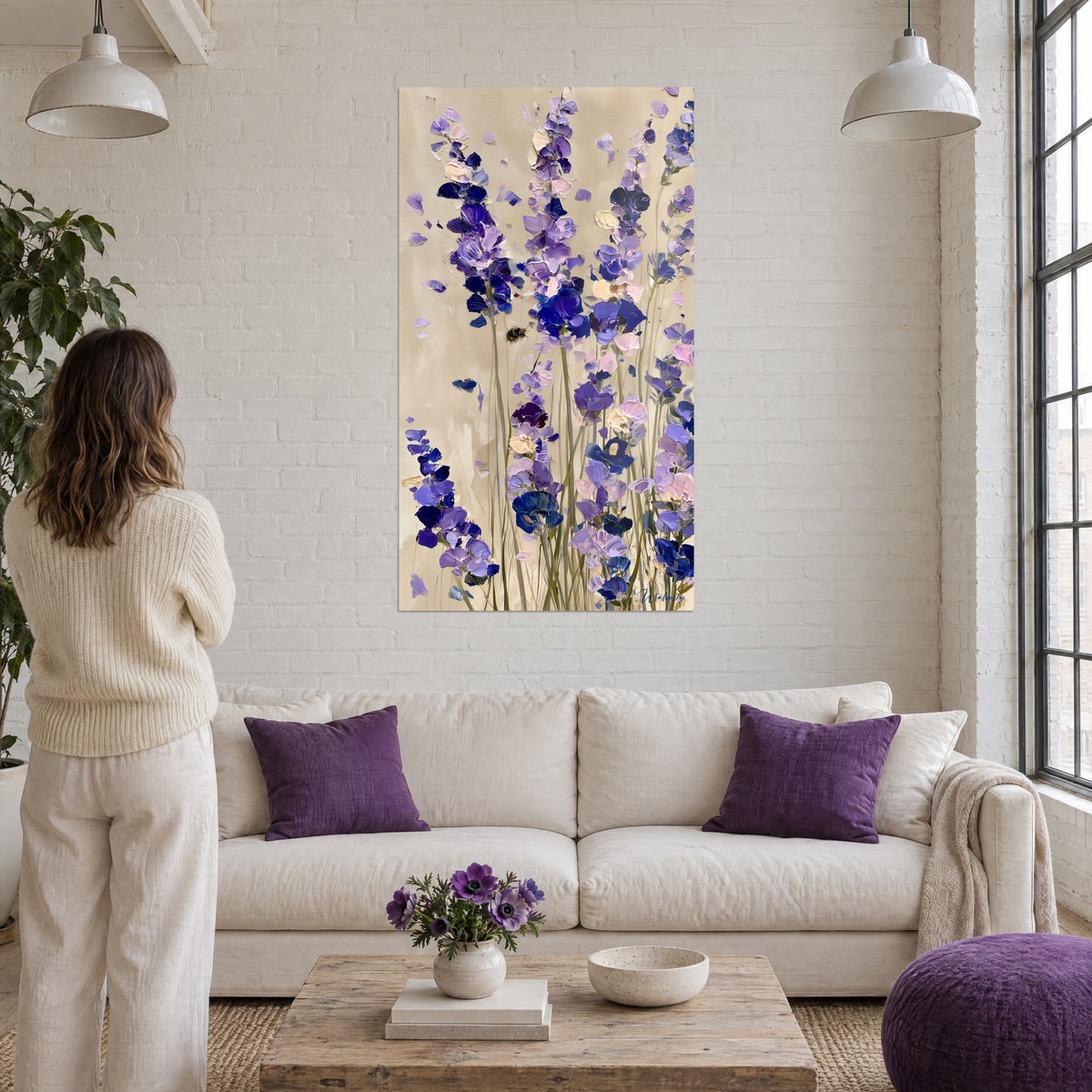 Quadro spighe di lavanda viola su fondo beige sabbia, ape in volo, donna di spalle, sopra un divano in un soggiorno luminoso