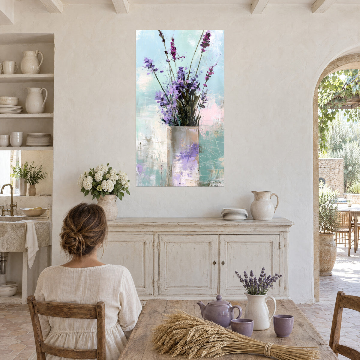 Quadro spighe viola e fogliame scuro dipinti a spatola, vaso rosa, sfondo turchese, di fronte a un tavolo di casolare provenzale