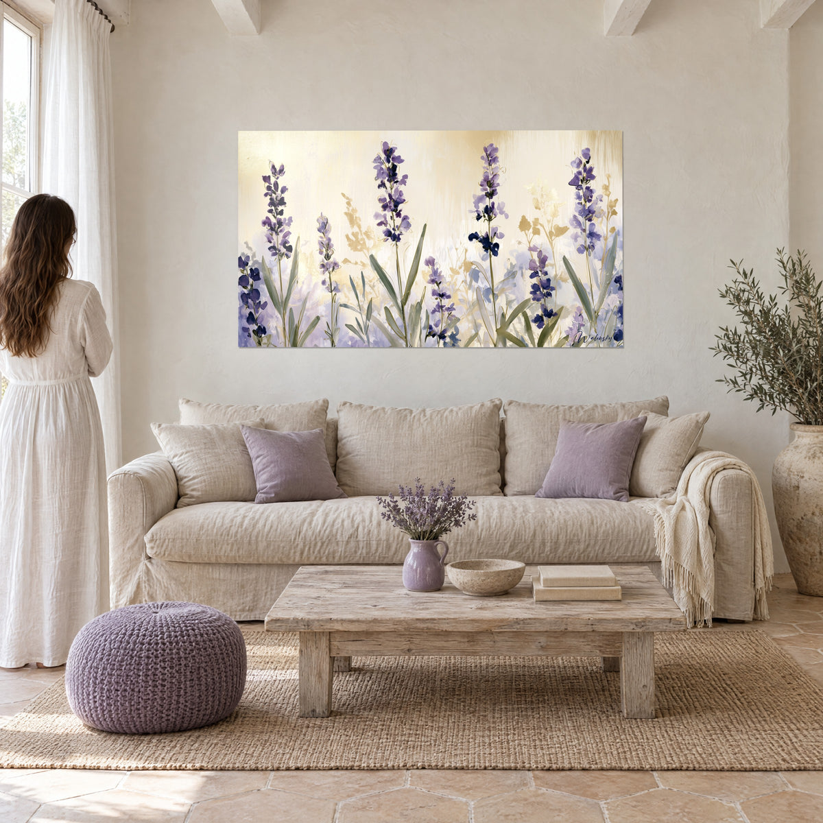 Quadro spighe di lavanda viola su fondo oro pallido, foglie verde salvia, donna in abito bianco di spalle, sopra un divano in un soggiorno luminoso