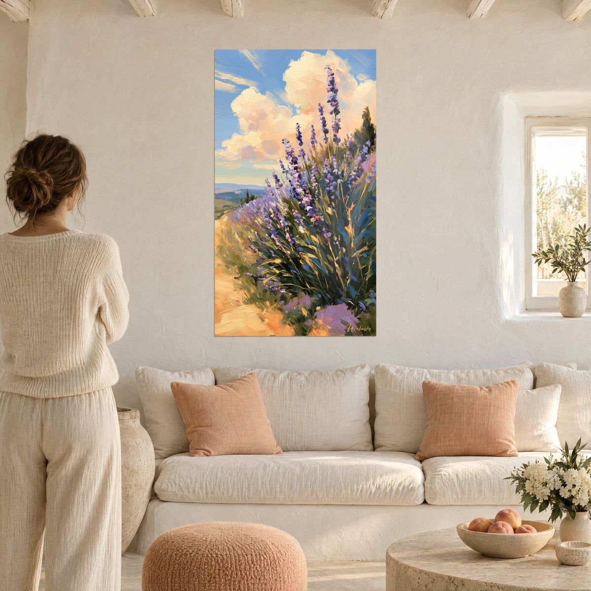 Wall art purple lavender spikes under large cream clouds against a blue sky, woman seen from behind, above a sofa in a bright living room