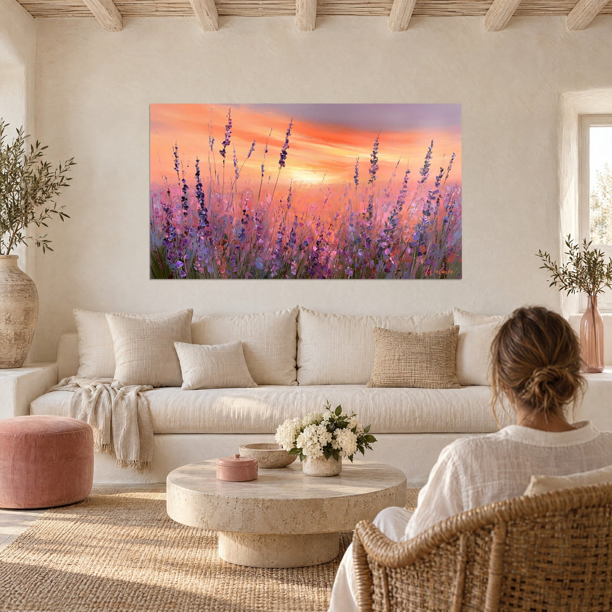 Wall art lavender field in bloom, purple spikes against an orange and pink sky, person seen from behind, hanging above a sofa in a bright living room