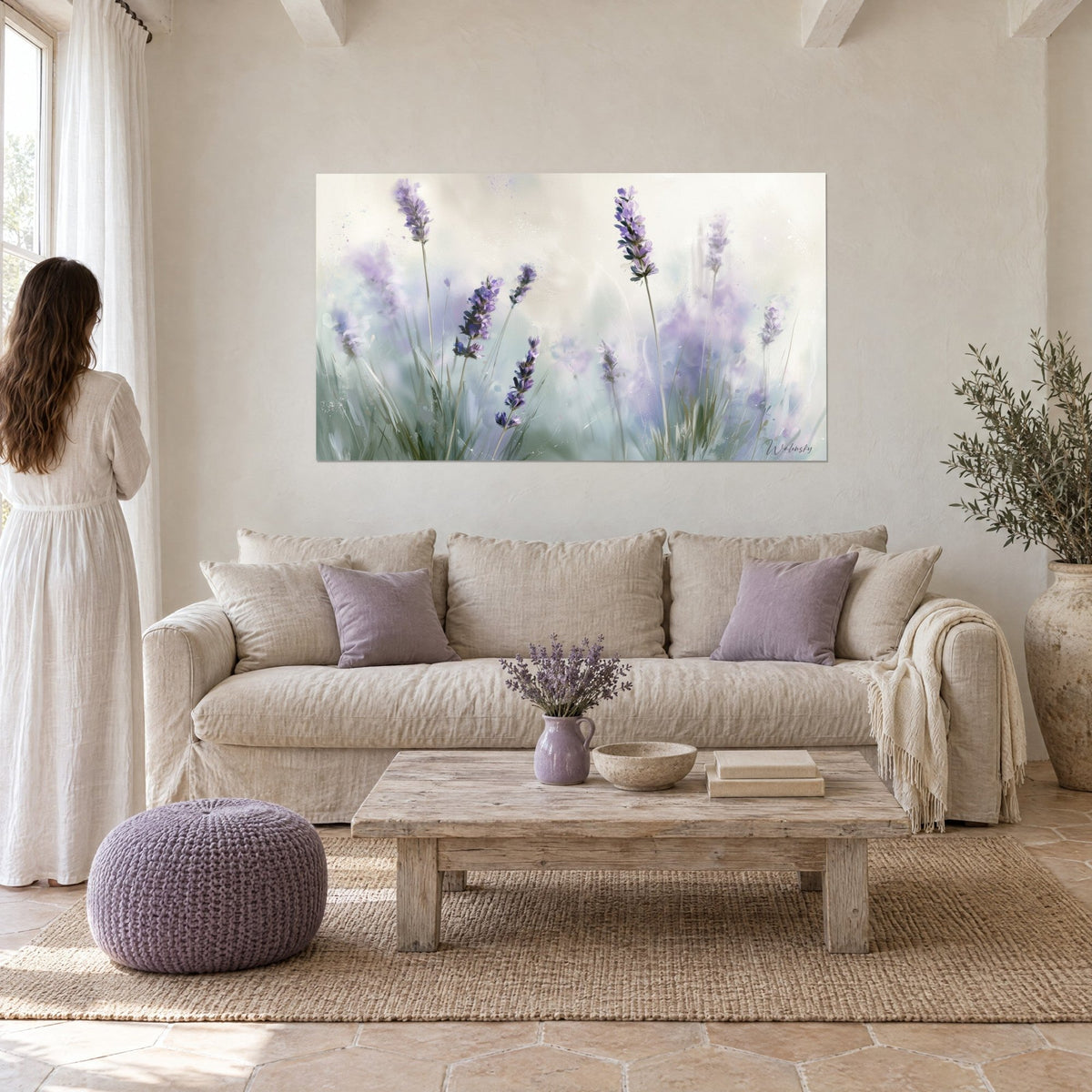 Cuadro espigas de lavanda morada en una bruma salvia, tallos finos y fondo crema; mujer de espaldas sobre un sofá en un salón luminoso