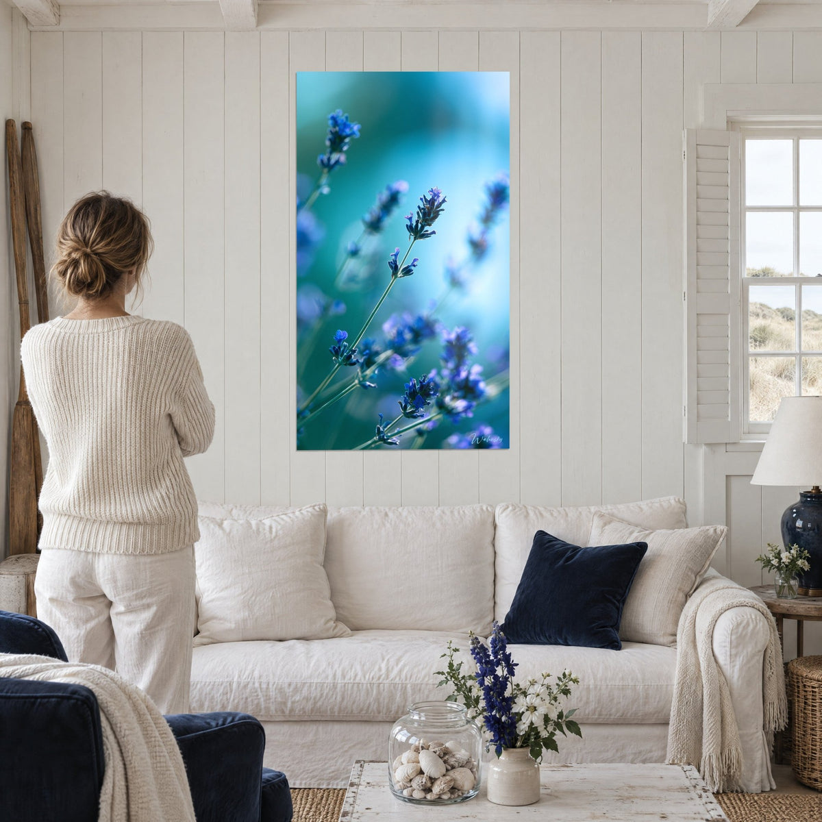 Wall art purple lavender spikes on blurred turquoise background, woman seen from behind, above a sofa in a bright living room