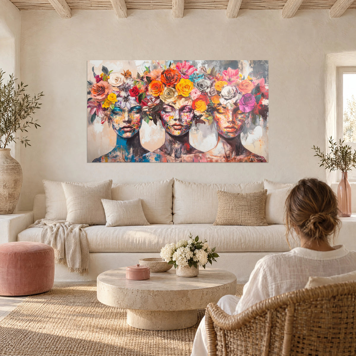 Wall art three female faces with closed eyelids, crowned with orange and yellow roses, above a sofa in a bright living room