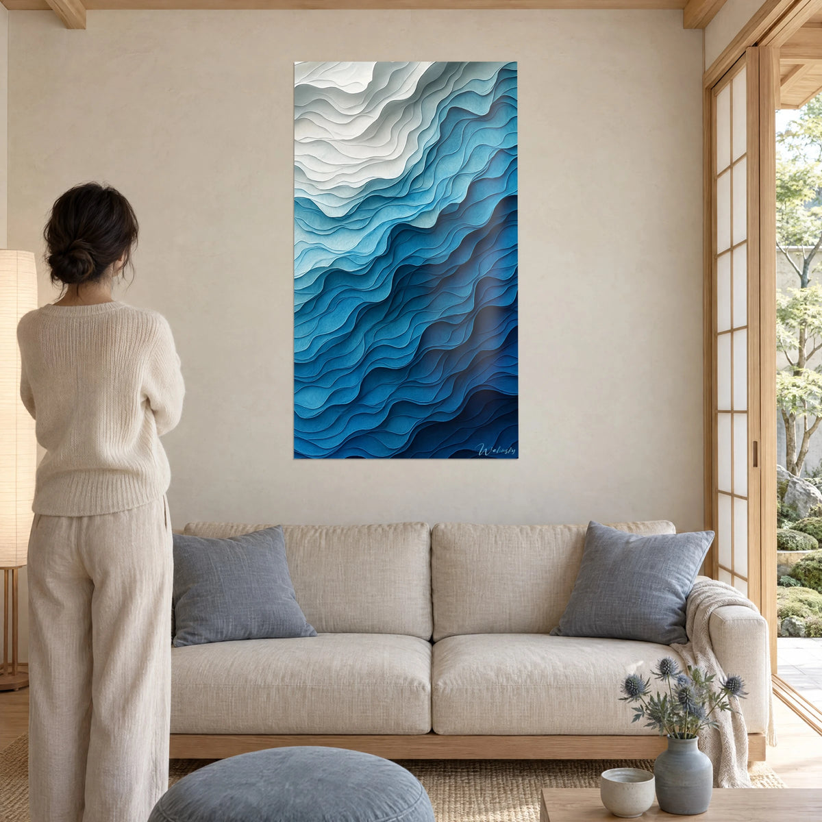 Schilderij met overlappende papieren golven, parelmoerwit en cyaanblauw, vrouw van achteren boven een bank in een lichte woonkamer