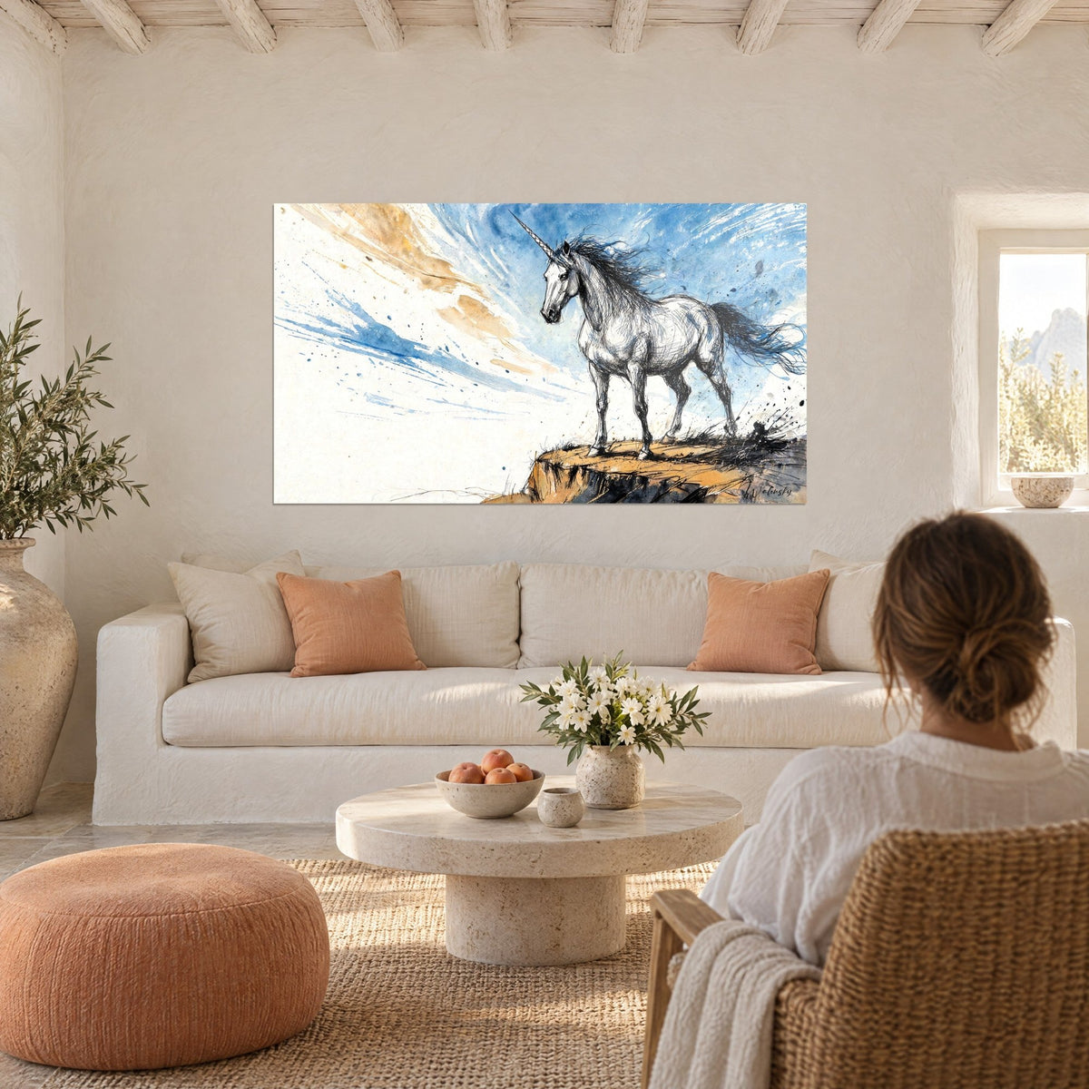 Quadro unicorno bianco dal manto punteggiato d'inchiostro, cielo blu e ocra, una donna di spalle, sopra un divano in un soggiorno luminoso