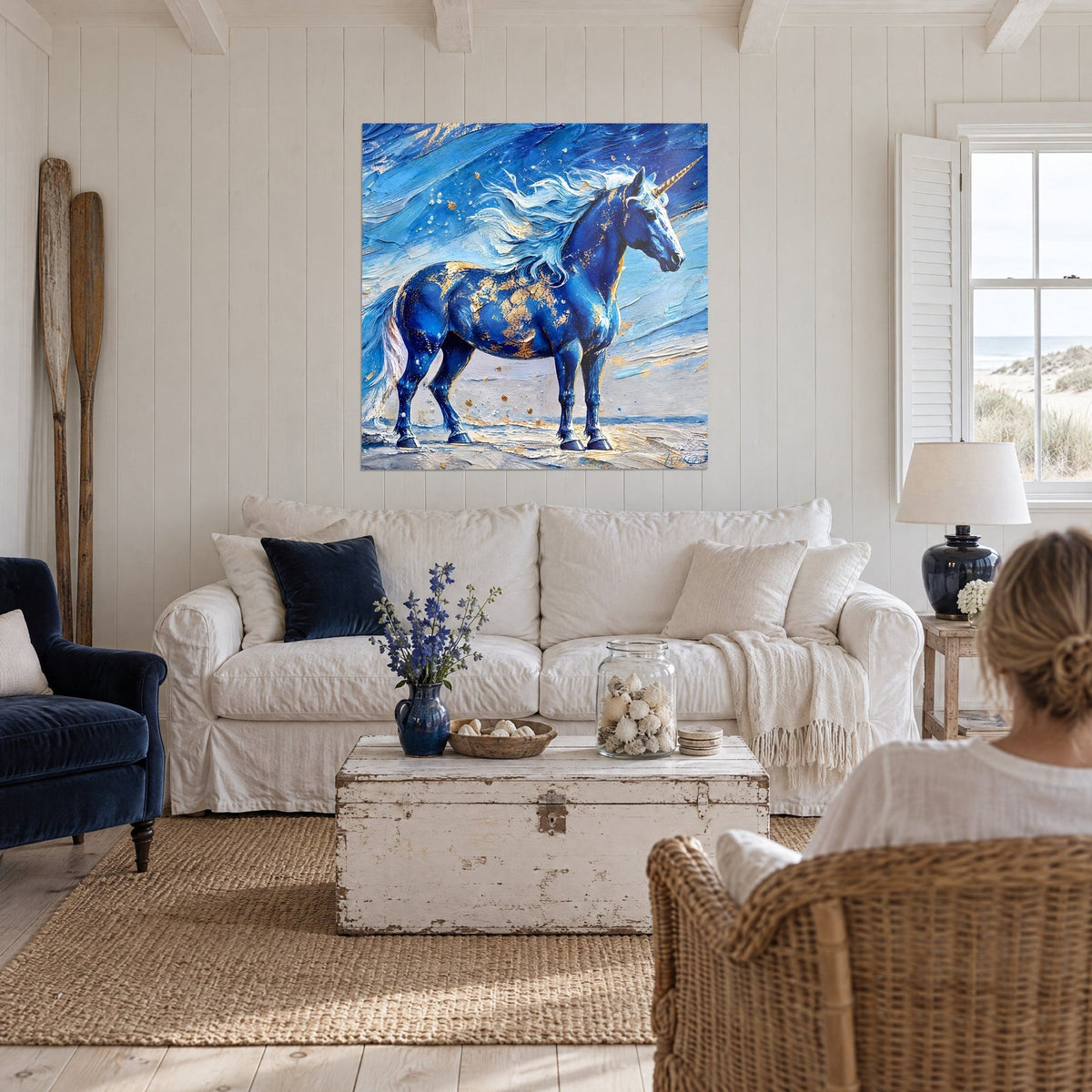 Wall art navy blue unicorn with white mane and golden sparkles, view of a woman from behind above a sofa in a bright living room