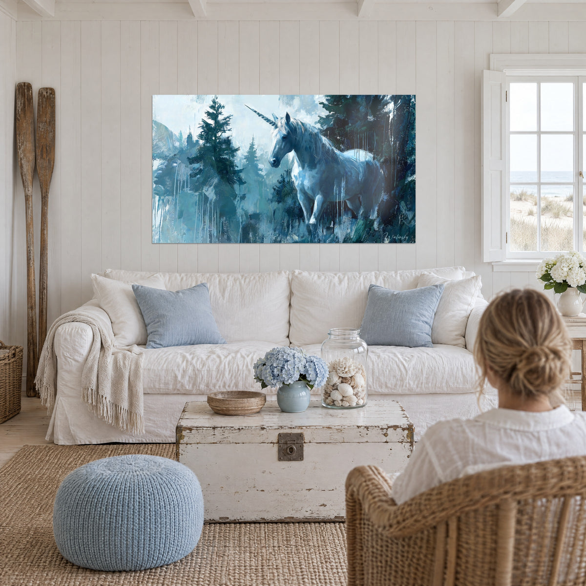Tableau licorne blanche à la corne spiralée dans une forêt bleu glacier et vert sapin, au-dessus d'un canapé dans un salon lumineux