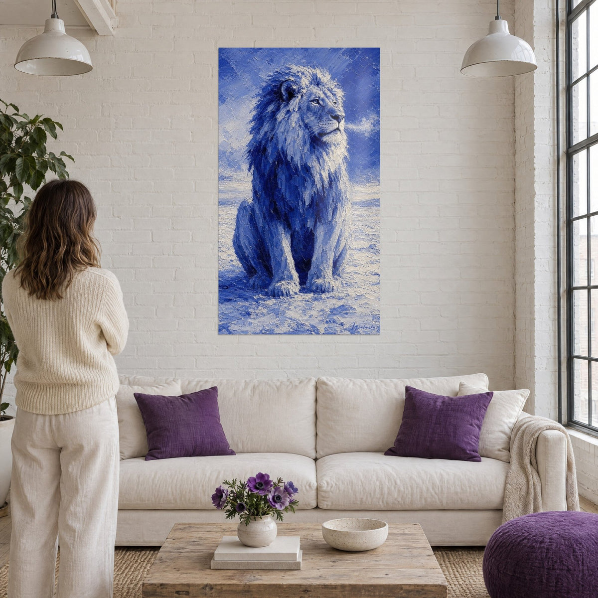 Gemälde Löwe sitzend mit indigoblauer und kreideweißer Mähne, Blick in die Ferne gerichtet, über einem Sofa in einem hellen Wohnzimmer