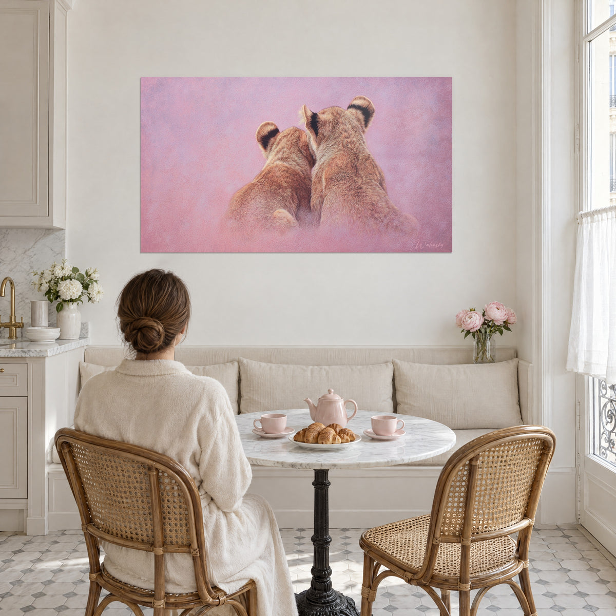 Schilderij van jonge leeuwen schouder aan schouder, koperkleurige vacht, levendig roze en mauve waas, tegenover een vrouw aan tafel in een crèmekleurige trui