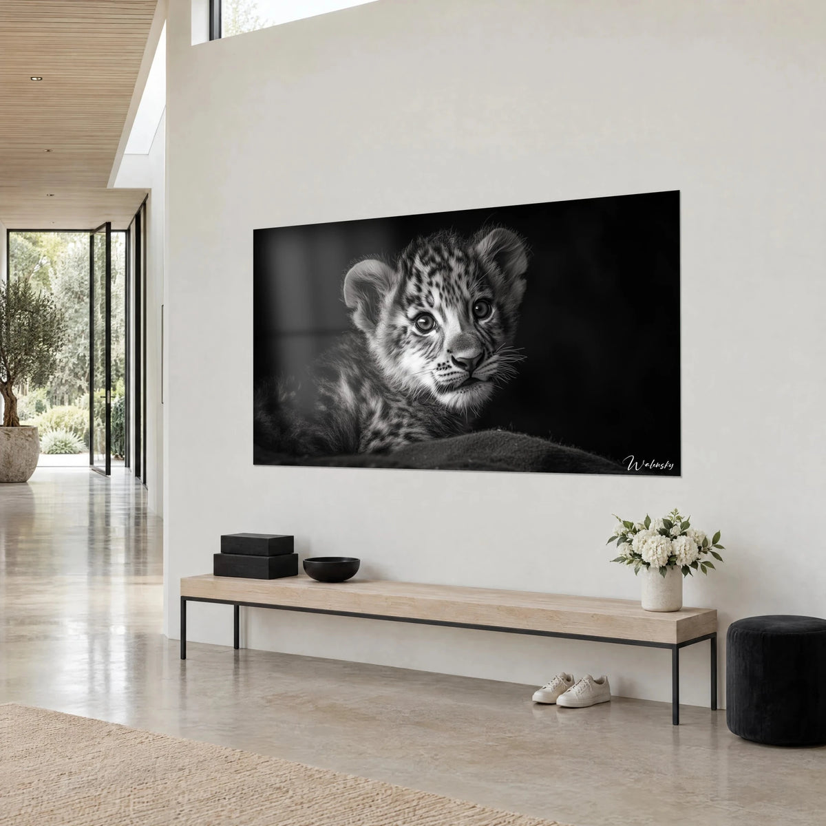 Quadro di un piccolo felino maculato in bianco e nero, muso rosa pallido e baffi chiari, sopra una panca in legno chiaro