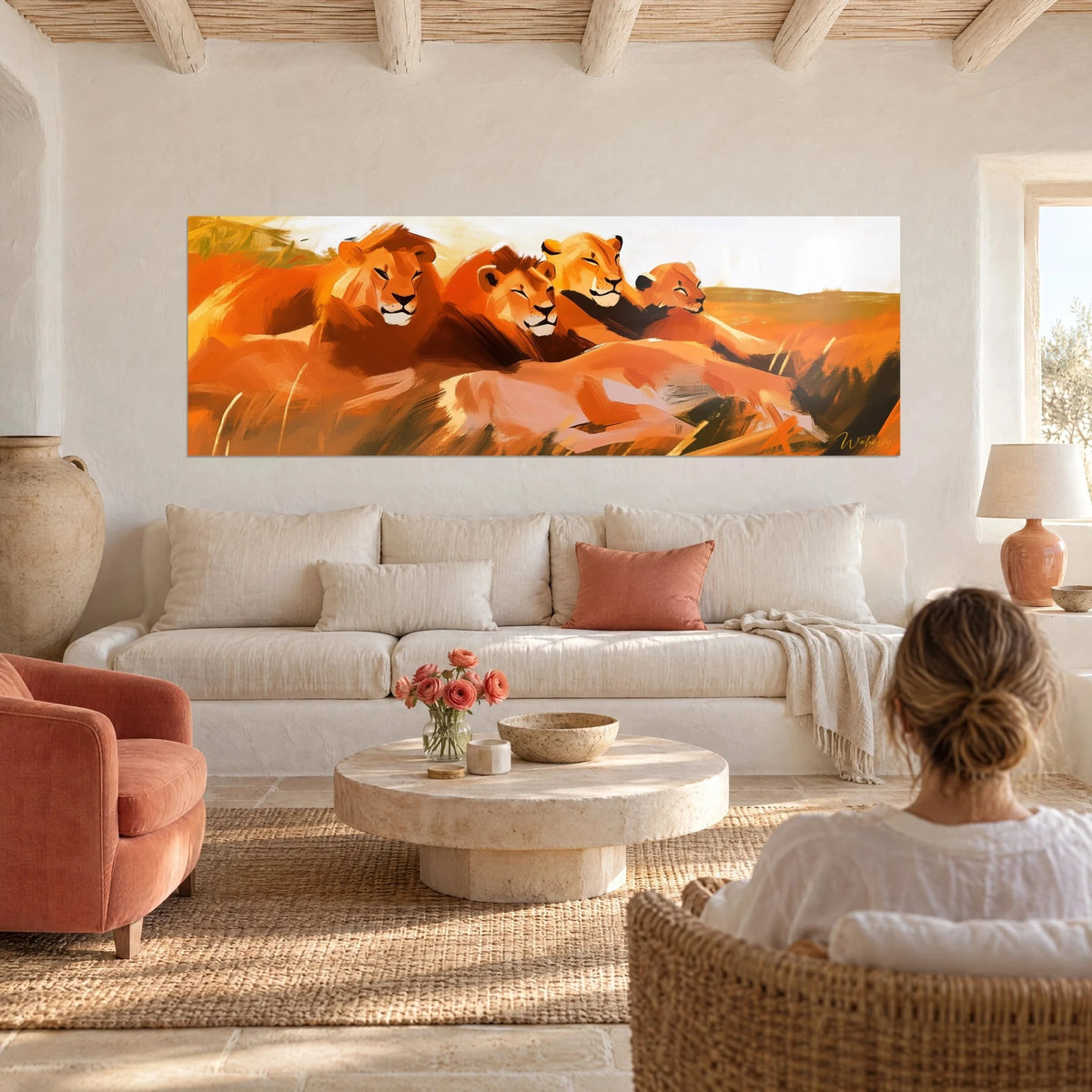 Gemälde Löwen als Familie liegend, kupferfarbene Mähnen und cremefarbener Himmel, eine Frau von hinten über einem Sofa in einem hellen Wohnzimmer