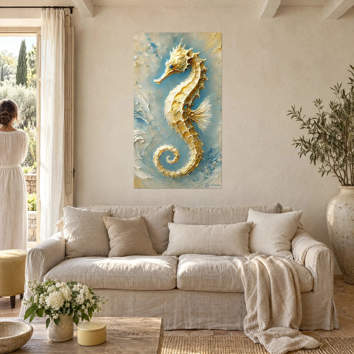 Schilderij gouden reliëf zeepaardje op hemelsblauwe achtergrond, een vrouw van achteren op de voorgrond, boven een bank in een lichte woonkamer