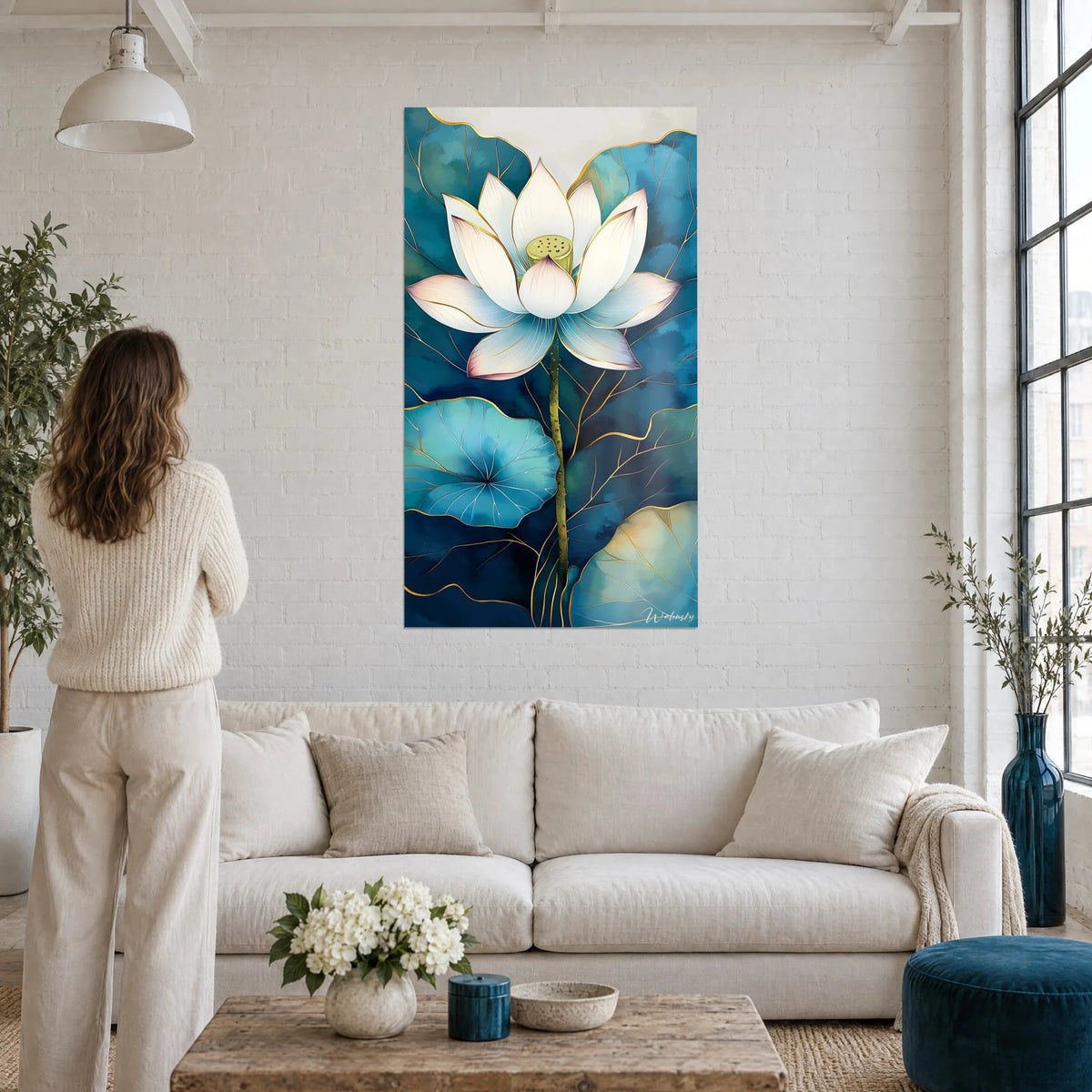 Tableau fleur de lotus blanc aux pétales rosés, feuilles bleu turquoise et filets dorés, au-dessus d'un canapé dans un salon lumineux