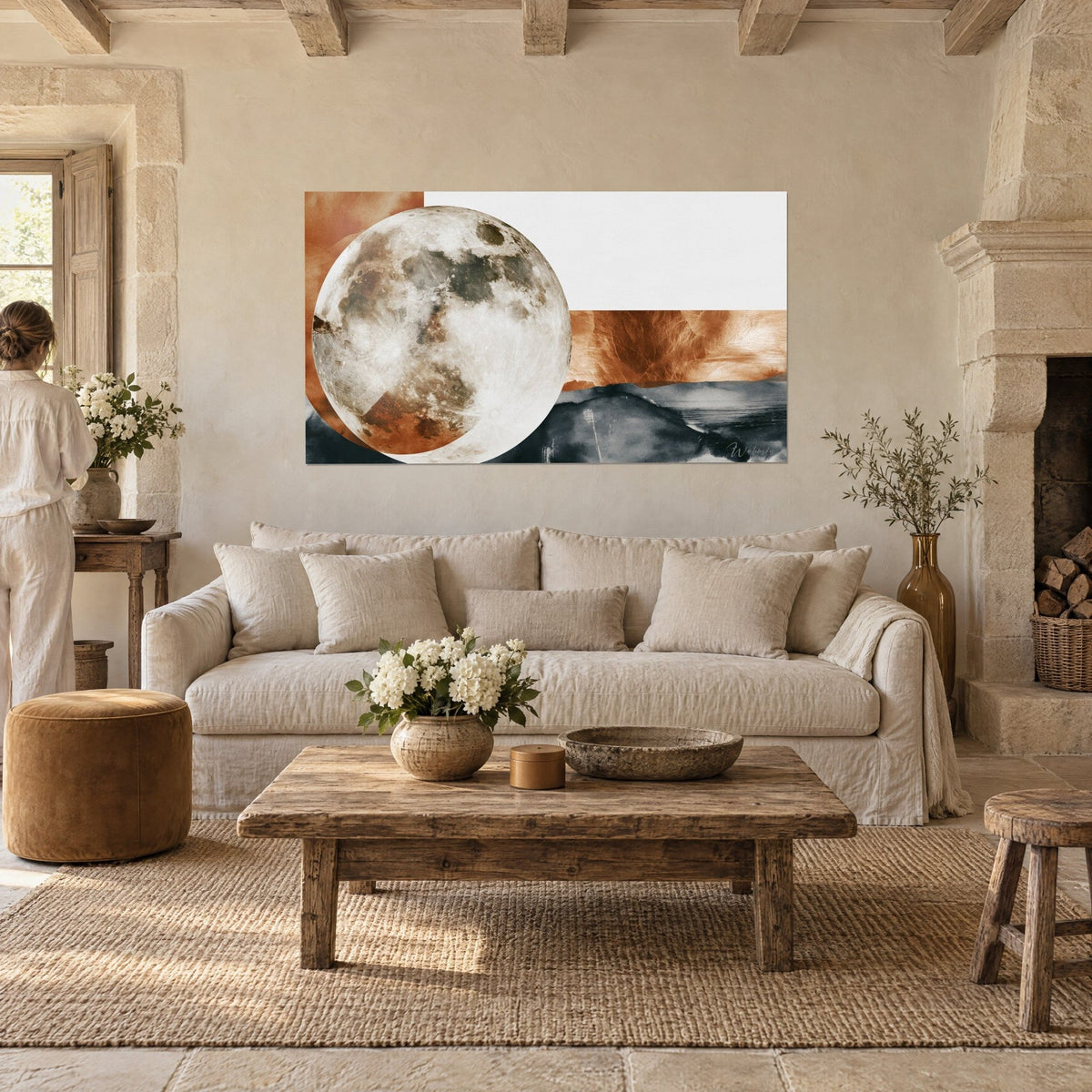 Schilderij volle maan met kraters op vlakke terracottakleurige achtergrond en antracietkleurige heuvels, vrouw van achteren, boven een bank in een lichte woonkamer