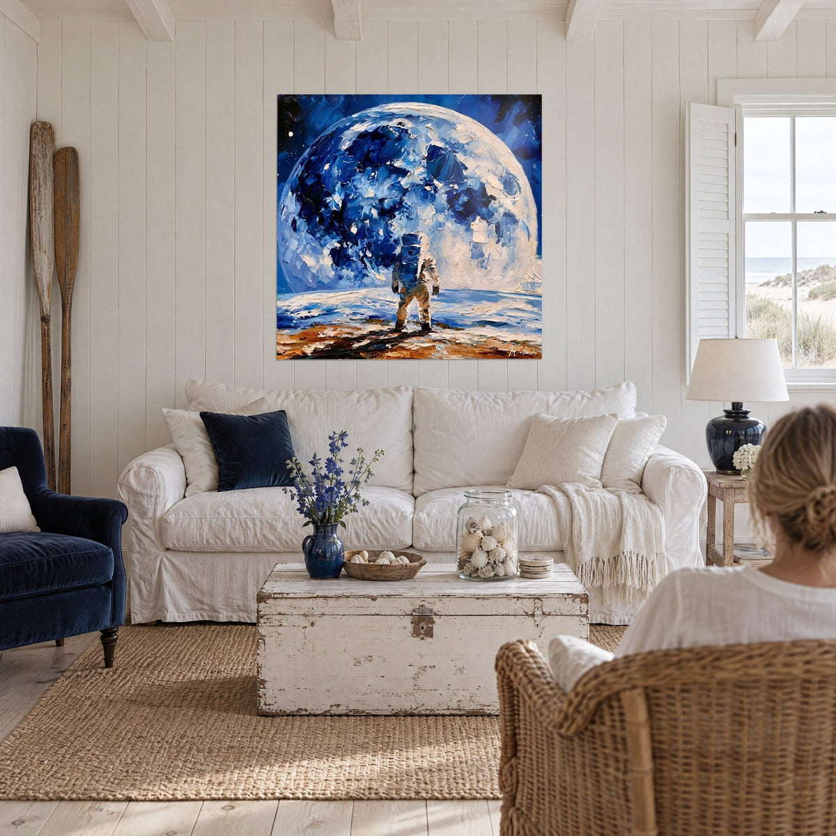 Wall art astronaut in front of a giant blue moon, indigo and cream impasto strokes, above a sofa in a bright living room