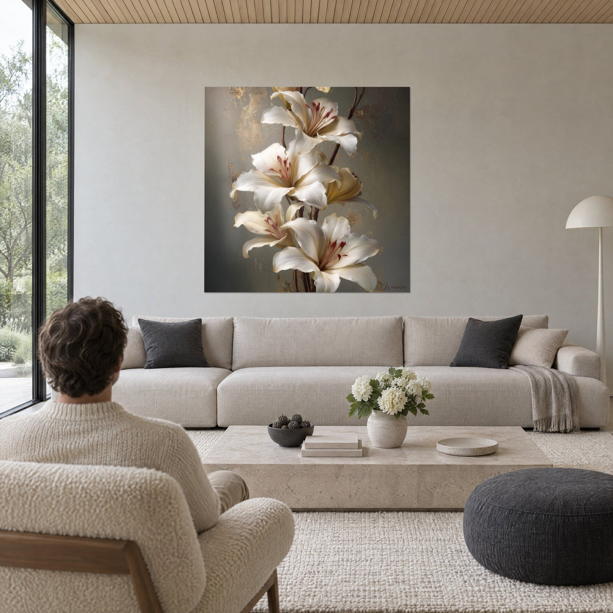 Tableau bouquet de lys blancs aux étamines rouges sur fond gris-vert patiné d'or, au-dessus d'un canapé dans un salon lumineux