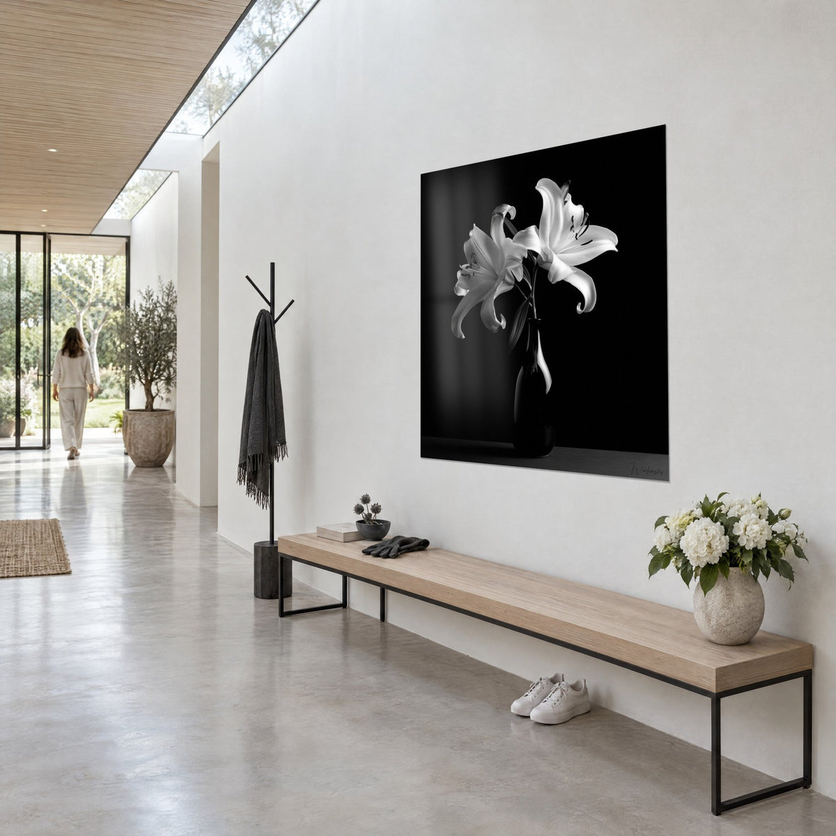 Tableau bouquet de lys ivoire en noir et blanc, étamines sombres, vase ébène, mur clair d'un couloir vitré, vue de trois-quarts
