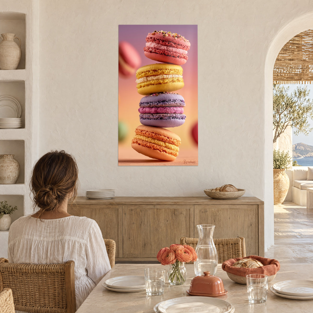 Wall art column of macarons with pink, white and fuchsia creams, pistachio crumbs, a woman seen from behind seated at a dining table