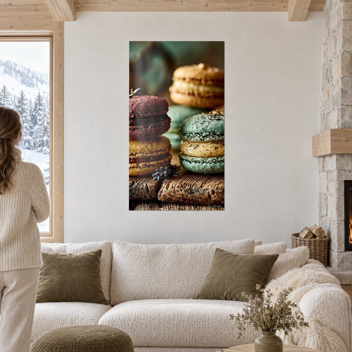 Quadro con macarons impilati bordeaux e pistacchio su legno scuro, rametti di lavanda, visti di spalle da due persone sopra un divano in un soggiorno luminoso