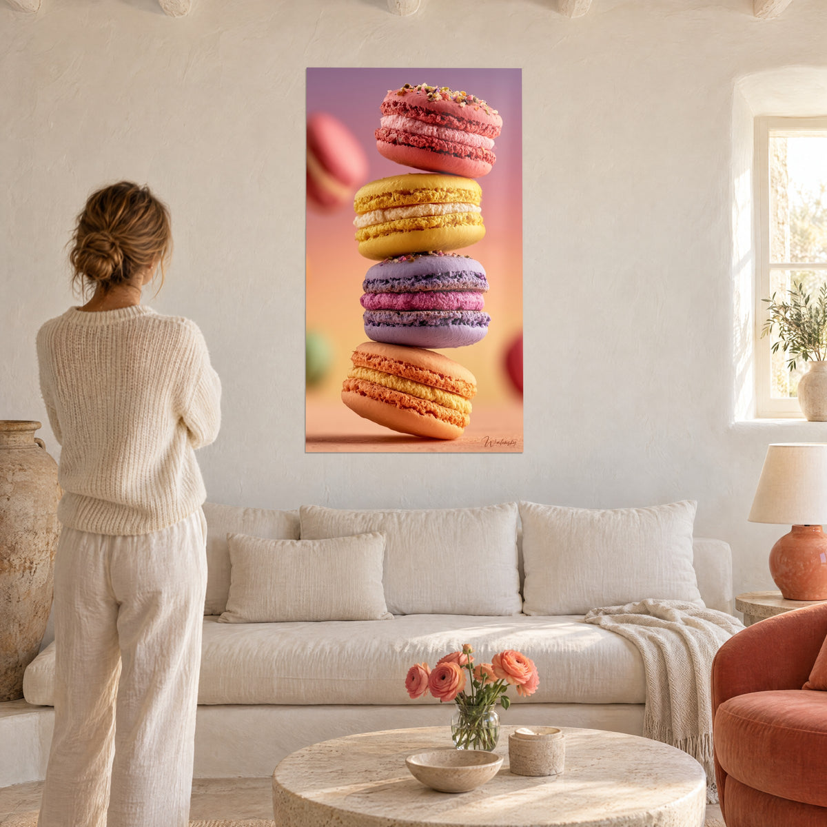 Wall art tower of pink, yellow, mauve and apricot macarons in balance, a woman seen from behind, above a sofa in a bright living room
