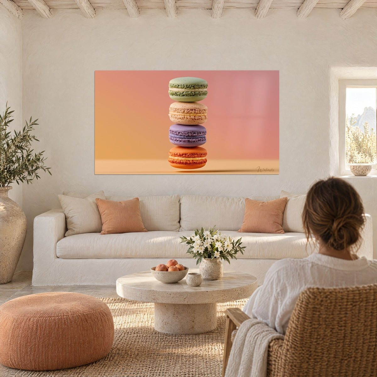 Tableau pile de quatre macarons vert pistache, beige, lavande et orange sur fond rose, au-dessus d'un canapé dans un salon lumineux