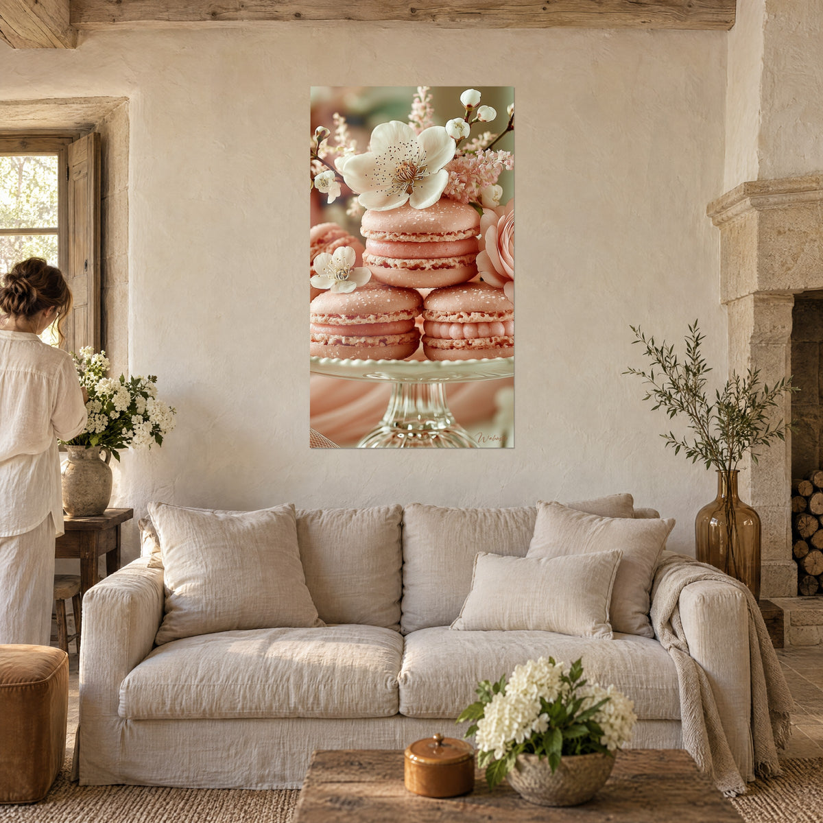 Tableau macarons rose pâle empilés sous une fleur de pommier ivoire, une femme de dos, au-dessus d'un canapé dans un salon lumineux