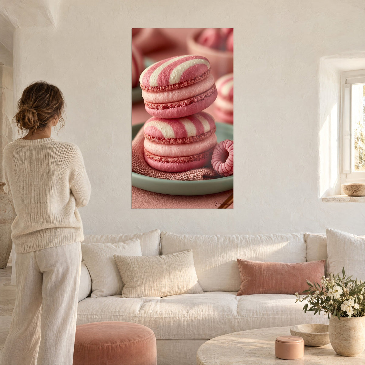 Quadro macarons impilati a righe rosa e crema su piatto celadon, donna di spalle, sopra un divano in un soggiorno luminoso
