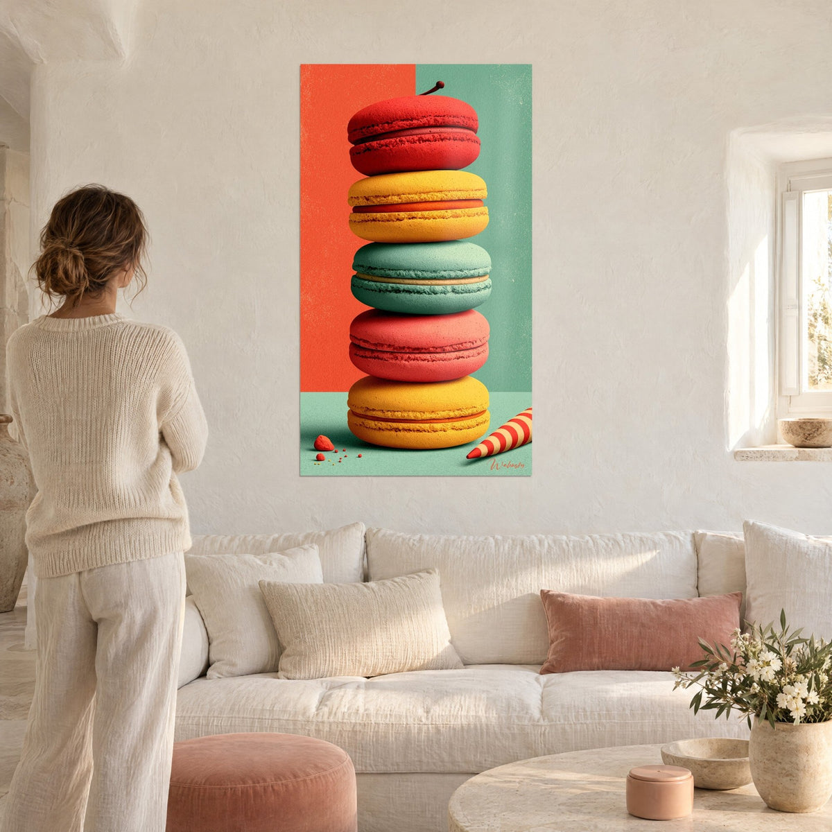 Tableau pile de cinq macarons rouge, jaune et vert menthe sur fond corail, une femme de dos, au-dessus d'un canapé dans un salon lumineux