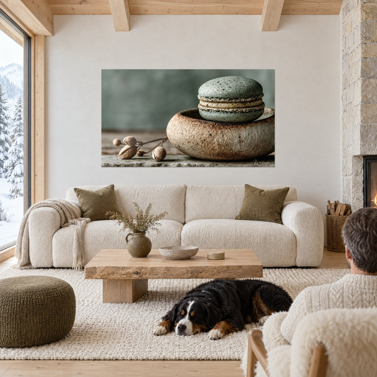 Tableau macaron sauge fourré de crème beige, posé sur un bol en grès, face à un chien noir couché, au-dessus d'un canapé dans un salon lumineux