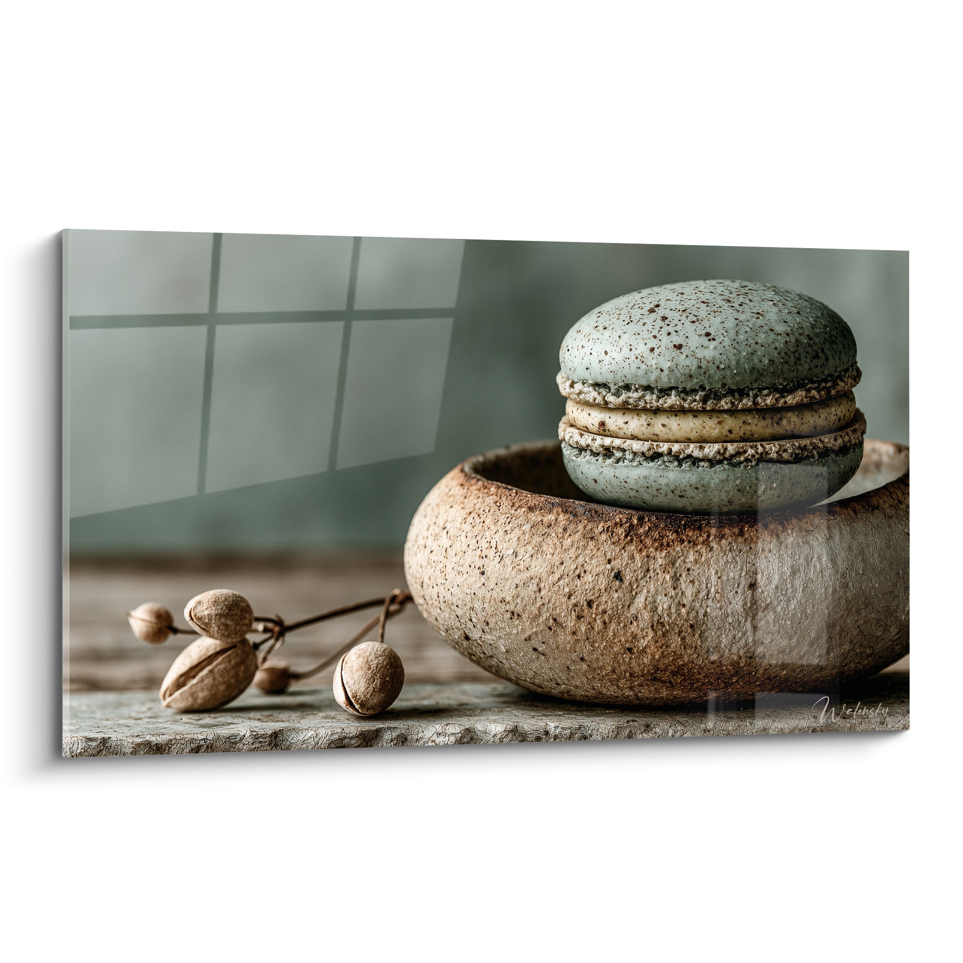 Macaron vert sauge moucheté posé sur bol en grès brun texturé, fond gris flouté