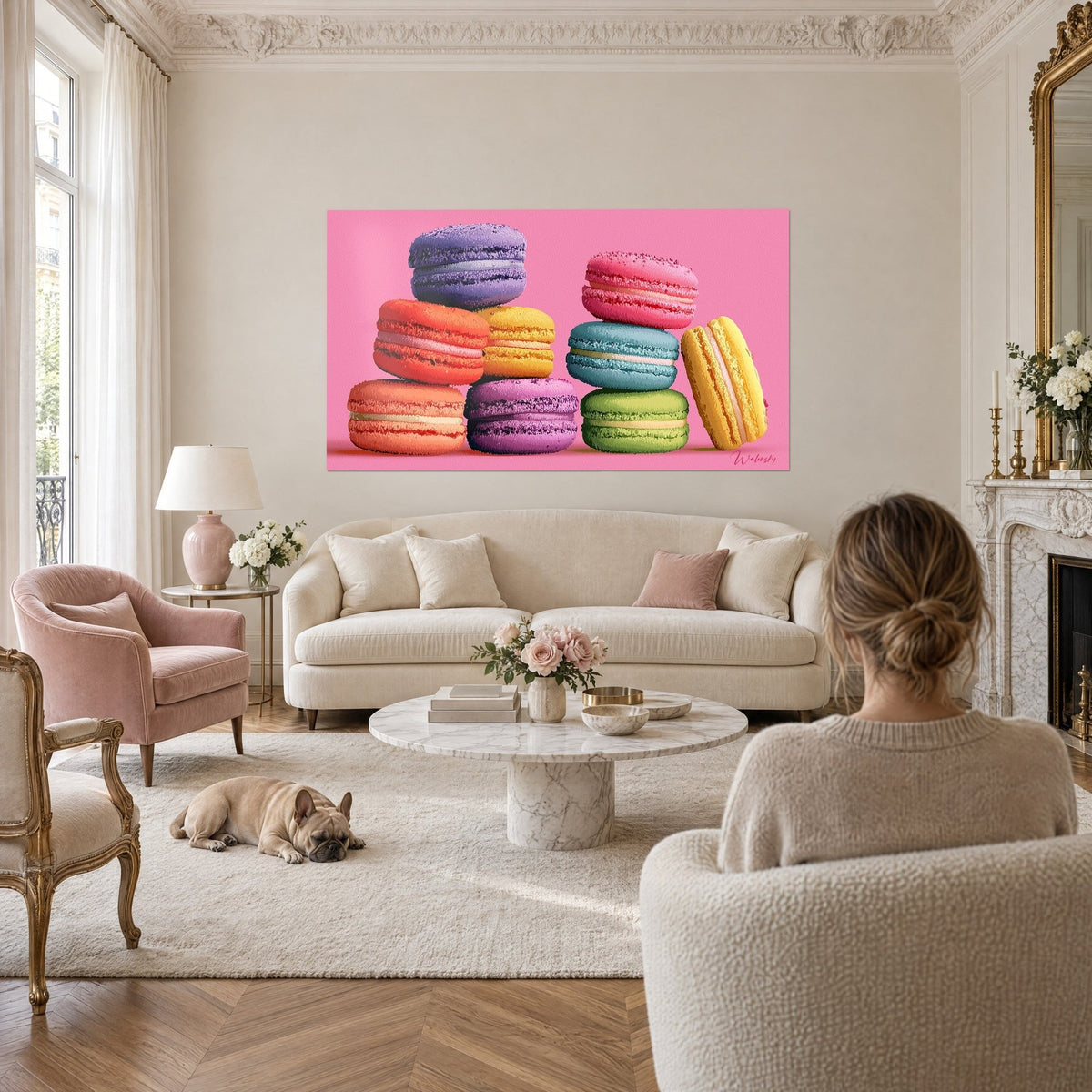 Tableau pile de macarons pop violet et orange sur fond rose vif, femme de dos et bulldog, au-dessus d'un canapé dans un salon lumineux