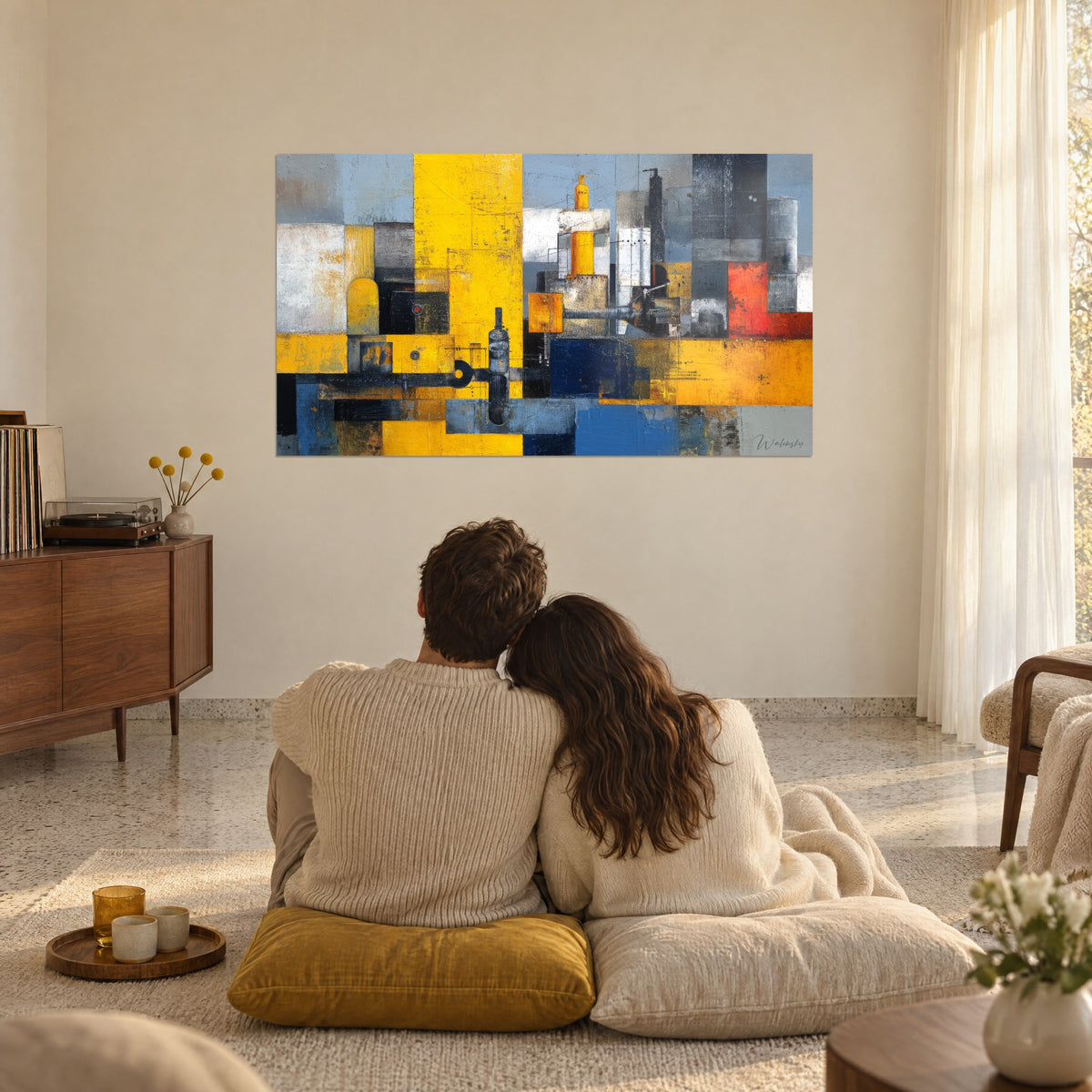 Cuadro ciudad mecánica abstracta en amarillo intenso y azul vaquero, trazos de raspado, una pareja abrazada de espaldas sentada sobre cojines, salón luminoso